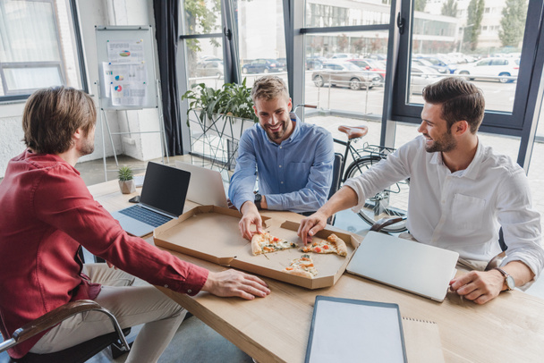 happy young businessmen eating pizza at workplace  - Photo, Image