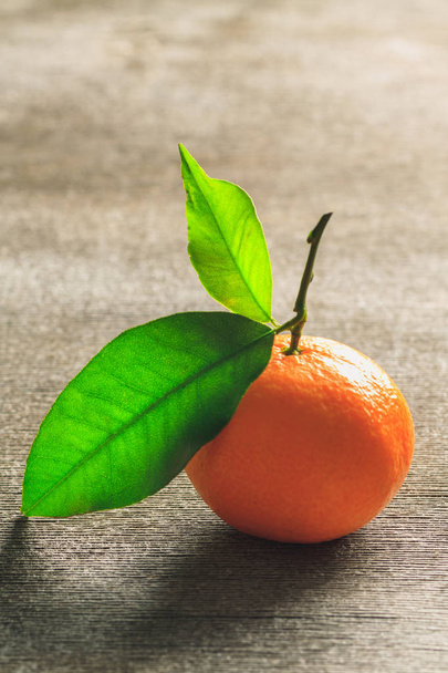 Одномісний мандарин в соковитому помаранчевому кольорі з зеленим листом на старовинному дерев'яному столі. Вертикальна орієнтація
. - Фото, зображення