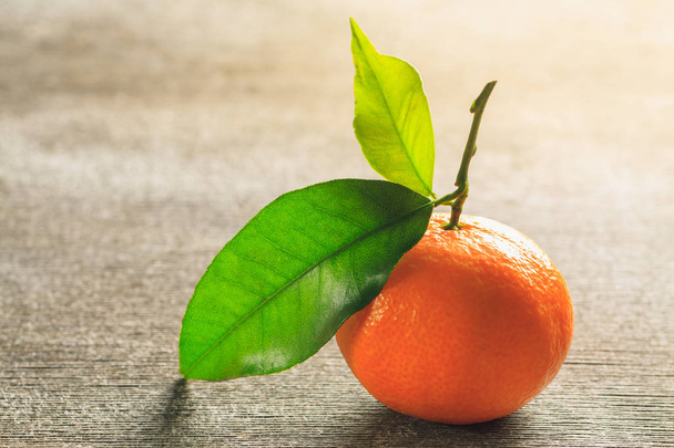 Одинокий мандарин сочного оранжевого цвета с зеленым листом на винтажном деревянном столе. Горизонтальная ориентация
. - Фото, изображение