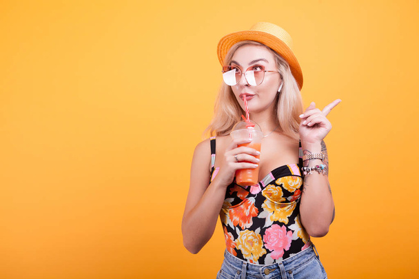Hermosa joven bebiendo jugo de naranja fresco con gafas de sol y sombrero
 - Foto, imagen