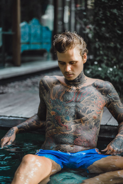 fiatal jóképű férfi tetoválásokat, a szabadtéri medencénél pihen. A tetovált ember a medencében jól szórakozik. a Bali szigetén, Indonézia - Fotó, kép
