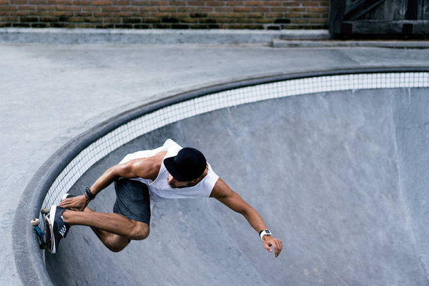 A stylish young man in a white T-shirt and cap skates on a skateboard in a skatepark, skating in a pool. - Foto, imagen