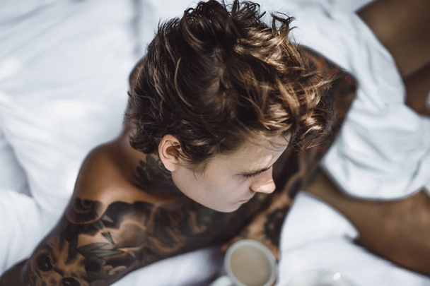 Handsome young tattooed man relaxing on white bed - Foto, Imagem