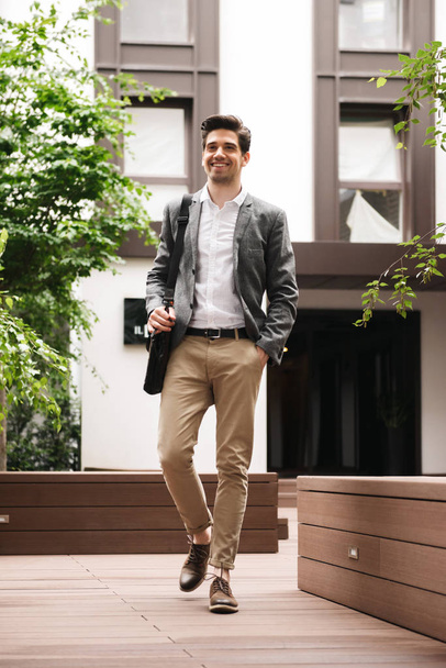 Full length of a smiling young businessman walking at the city - Photo, Image