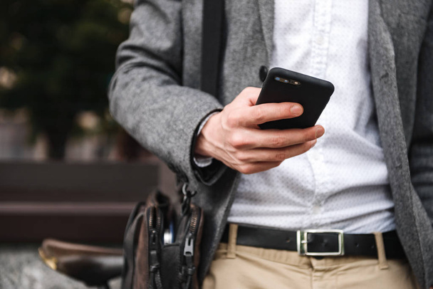 Close up of young businessman leaning on a wall while standing outdoors and using mobile phone - Foto, Imagen