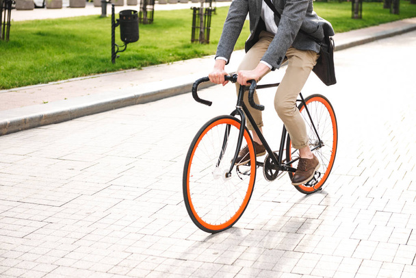 Cropped image of a young businessman riding on a bicycle on the city street - Photo, image