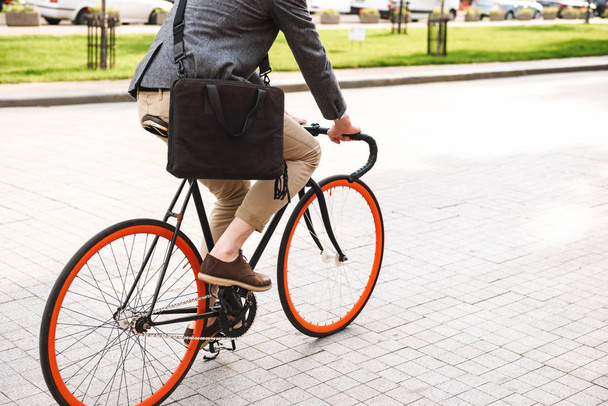 Cropped image of a young businessman with a bag riding on a bicycle on the city street - Foto, afbeelding