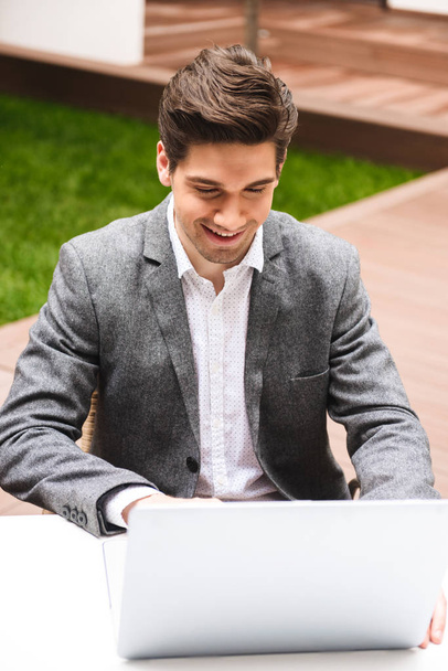 Attractive young businessman dressed in suit working on laptop computer while sitting outdoors - Photo, Image