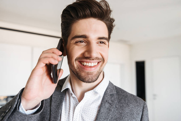 Close up of a smiling young man in suit talking on mobile phone at home - Photo, Image