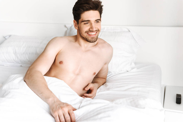 Hymyilevä paidaton mies makaa sängyssä kotona
 - Valokuva, kuva
