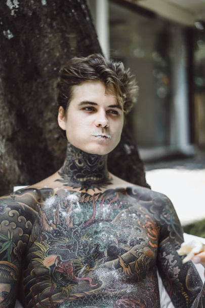 young handsome tattooed man having breakfast in bed in the open air outdoors in the garden - Foto, immagini