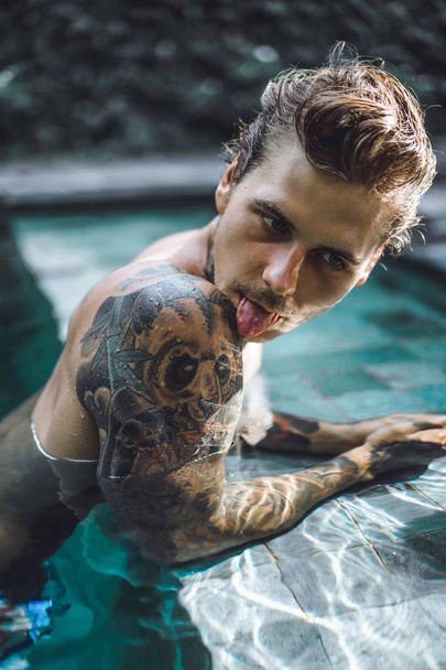 young handsome man in tattoos resting in the outdoor pool. A tattooed man in the pool is having fun. on bali, indonesia - Foto, afbeelding