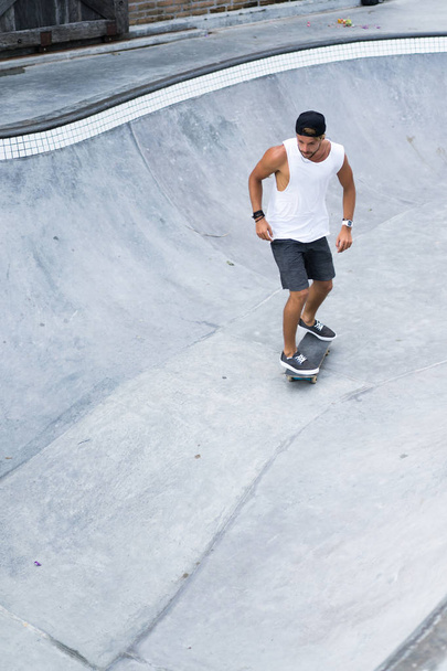 A stylish young man in a white T-shirt and cap skates on a skateboard in a skatepark, skating in a pool. - Φωτογραφία, εικόνα