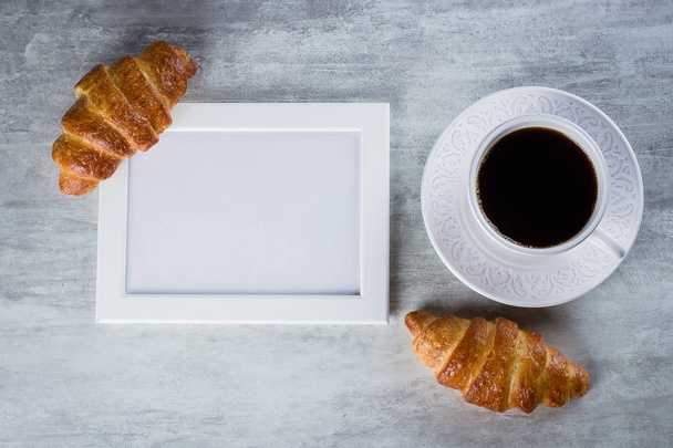 Blank white frame with copy space, cup of coffee and croissants on a grey table background. Mockup with copy space, top view - Fotoğraf, Görsel