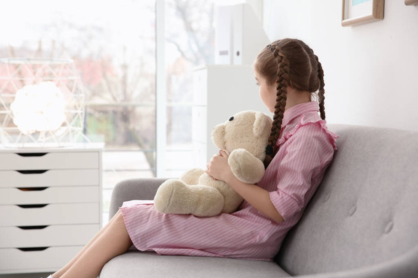Little autistic girl sitting on sofa with toy at home - Foto, afbeelding