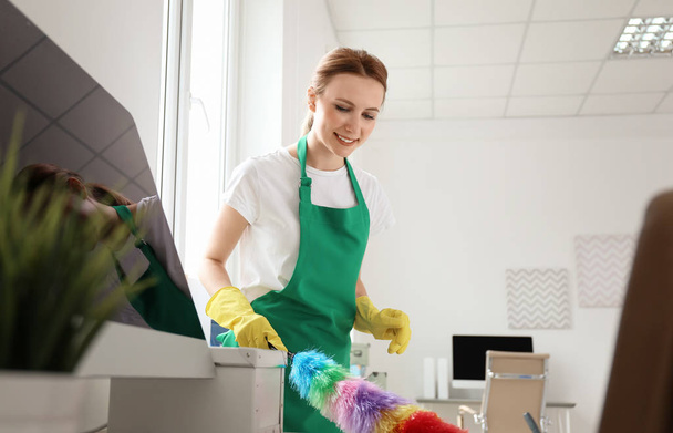 Young woman in apron and gloves cleaning office - 写真・画像
