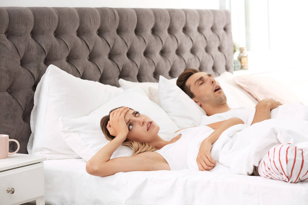 Young irritated woman lying on pillows in bed at home. Problem with snoring husband - Foto, Bild