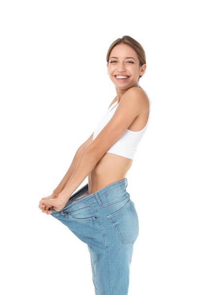 Young slim woman in old big jeans showing her diet results on white background - Φωτογραφία, εικόνα