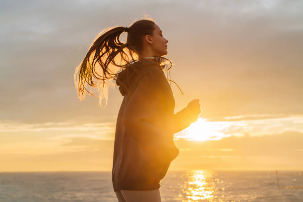 long-haired fast girl jogging along the seafront at sunset, wants to lose weight - Photo, Image