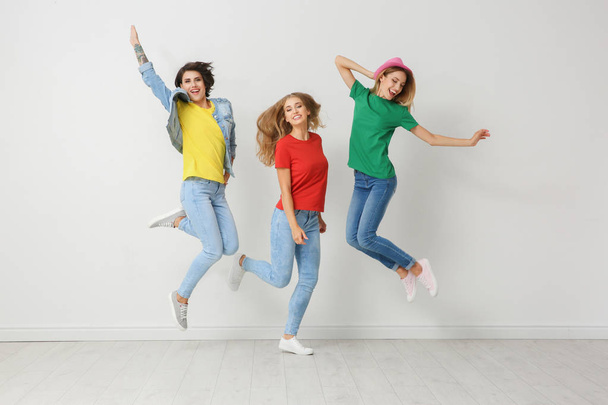 Group of young women in jeans and colorful t-shirts jumping near light wall - Photo, image