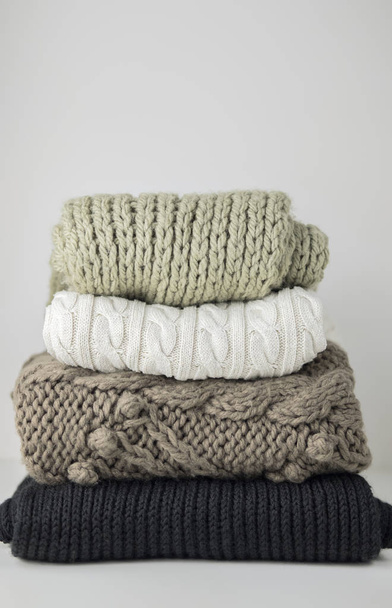 Warm woolen knitted winter and autumn clothes, folded in a pile on a white table. Sweaters, scarves. Place for text. Copyspace. - Fotoğraf, Görsel