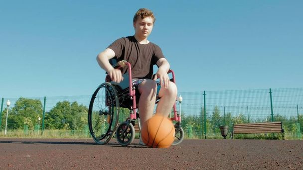 Vammainen mies pelaa koripalloa pyörätuolistaan, ulkona
 - Valokuva, kuva