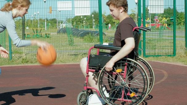 Gehandicapte man speelt basketbal van zijn rolstoel met een vrouw, op de open lucht, een inspanning leveren bij het afspelen van - Foto, afbeelding