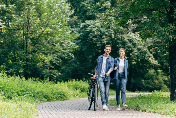 счастливая молодая пара прогуливаясь по парку с винтажным велосипедом
 - Фото, изображение