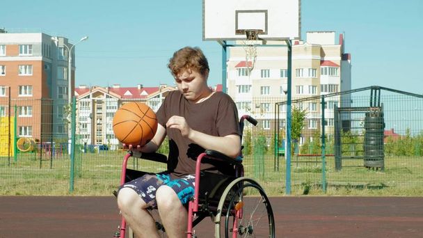 Gehandicapte man speelt basketbal van zijn rolstoel, op de open lucht, een inspanning leveren bij het afspelen van - Foto, afbeelding