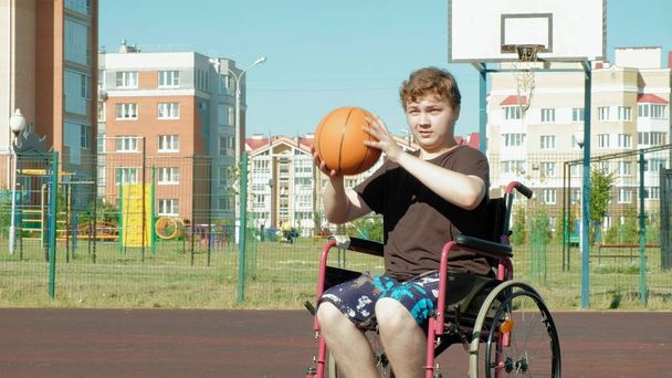Gehandicapte man speelt basketbal van zijn rolstoel, op de open lucht, een inspanning leveren bij het afspelen van - Foto, afbeelding