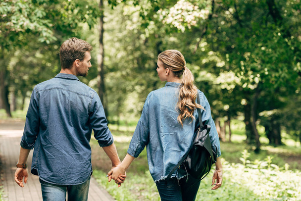 rear view of beautiful young couple in denim shirts walking by park - Fotó, kép
