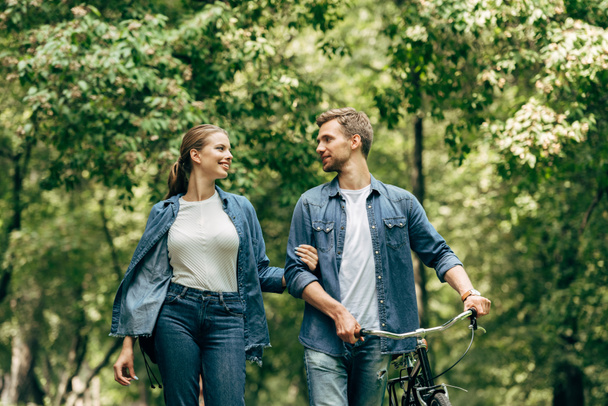 happy young couple in denim shirts with bicycle walking by park - Foto, Bild