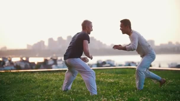 Zwei starke Männer zeigen im Sommer Elemente des Capoeira-Wrestlings auf dem Rasen - Filmmaterial, Video