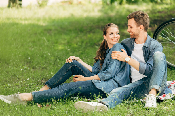feliz joven pareja sentado en la hierba en el parque juntos
 - Foto, imagen