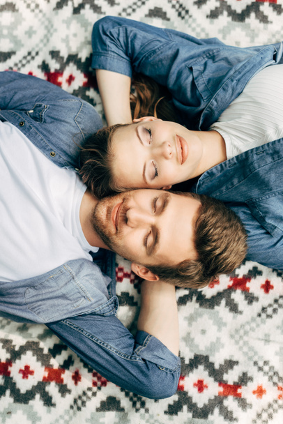 top view of beautiful young couple lying on patterned cloth with closed eyes - Photo, Image