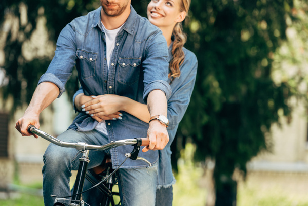 公園で一緒に自転車に乗って若いカップルのショットをトリミング - 写真・画像