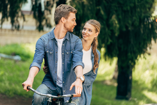 Schönes junges Paar fährt gemeinsam Fahrrad im Park und schaut sich einander an - Foto, Bild
