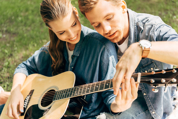 close-up shot of young happy woman learning to play guitar with boyfriend at park - Zdjęcie, obraz