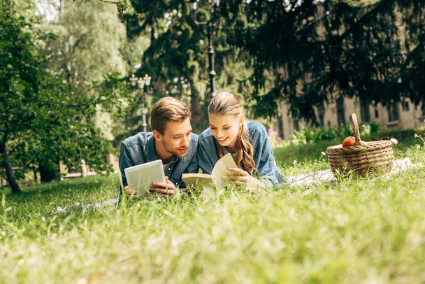 beautiful young couple lying on grass at park with tablet and book - Foto, immagini