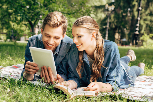 gelukkige jonge paar liggen op gras in het park en het gebruik van Tablet PC - Foto, afbeelding