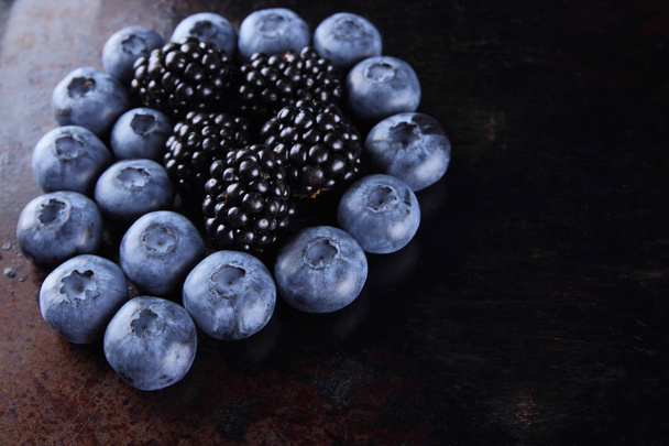 Blueberries and blackberries on dark background, fresh berries for vegan, fruits on rusty background, assorted berry breakfast - Foto, Bild