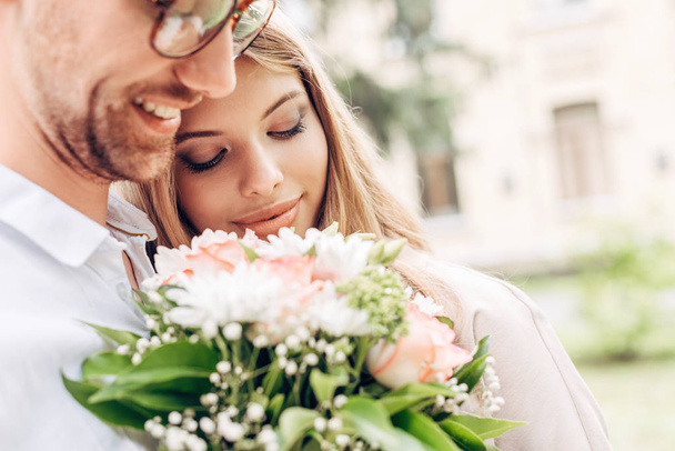 close-up shot of happy young couple with bouquet embracing outdoors - Foto, Imagem