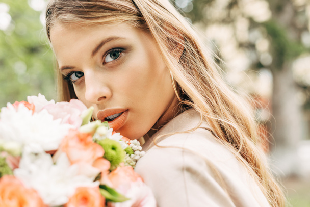 close-up portrait of beautiful young woman with flower bouquet looking at camera - Foto, afbeelding