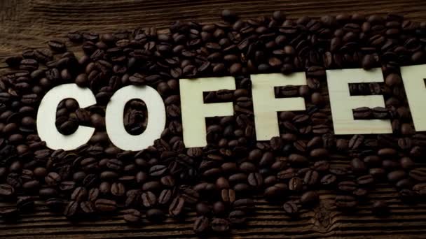 Schwarze Kaffeekörner liegen auf einem braunen Holztisch. das Wort Kaffee - Filmmaterial, Video