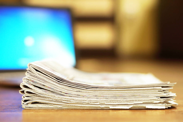 Des journaux pliés empilés à côté d'un ordinateur portable. Journaux tabloïds informatiques et quotidiens avec nouvelles, vue latérale
    - Photo, image