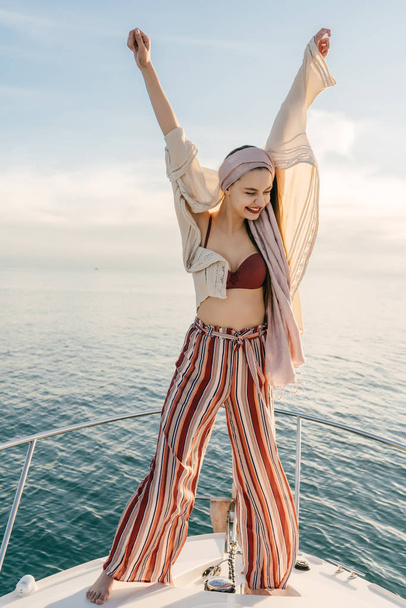 happy stylish girl is pleased with the long-awaited vacation, raised her hands up, on the yacht - Fotó, kép