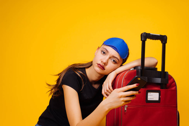 a tired young girl rests on her red suitcase, waits long for her plane, wants to leave - Foto, imagen