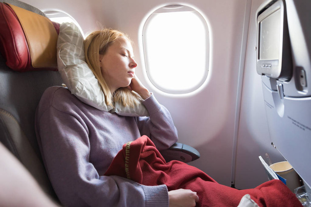 Tired blonde casual caucasian lady sleepin on seat while traveling by airplane. Commercial transportation by planes. - Photo, Image