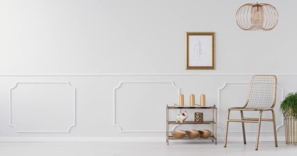 Video van een gouden stoel, rack met decoraties, planten op gouden stands en grijze muur met molding in heldere woonkamer interieur - Video