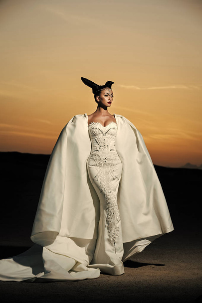 Girl posing on desert sunset sky. Woman in white wedding dress and gown. - Fotoğraf, Görsel
